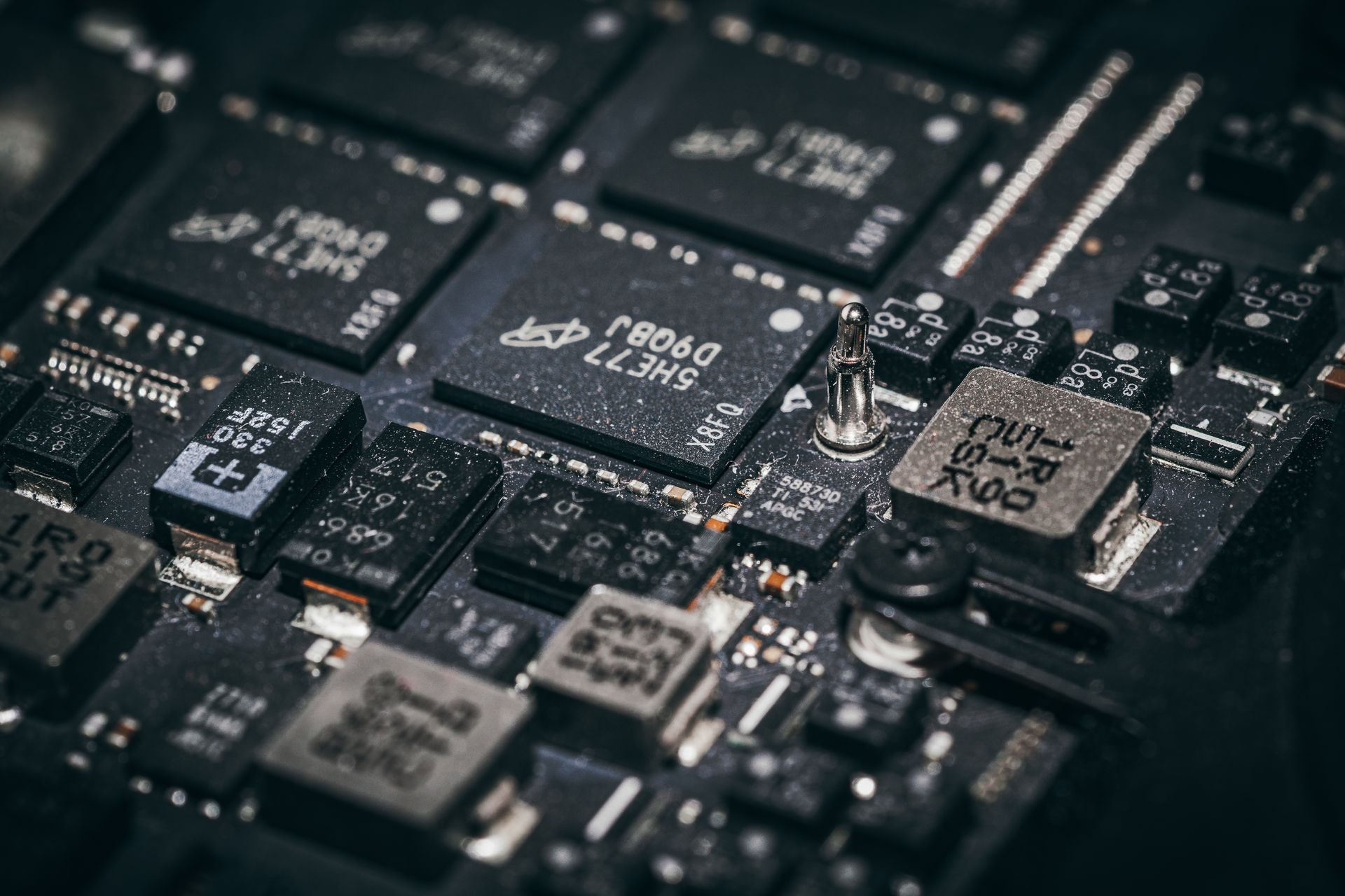 Macro photograph of a dark circuit board, chips labeled with alphanumeric designations